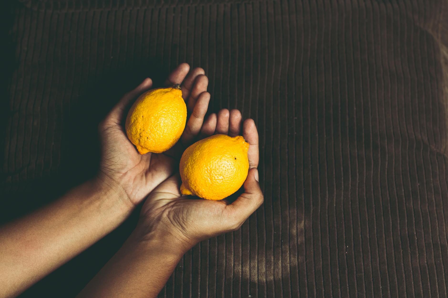 Close-up of a hand with white nails holding a fresh lemon on a soft pink background