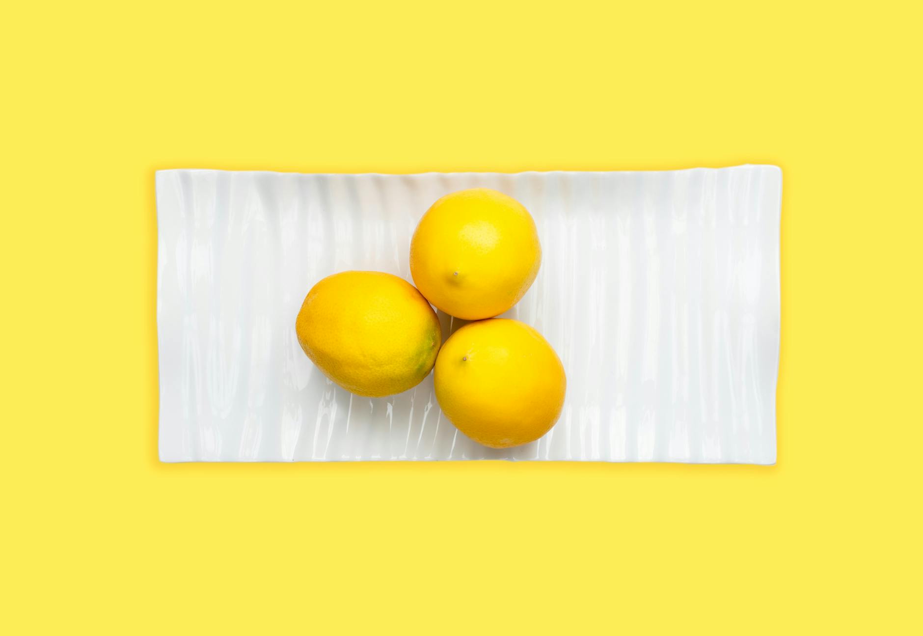 Fresh lemons arranged on a white plate against a yellow background, symbolizing the transition to lemon clitoral vibrators