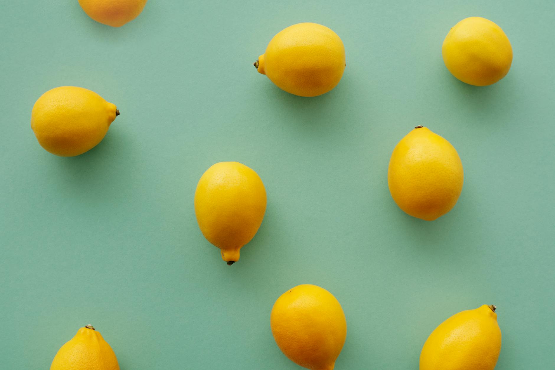 Hand holding a lemon on soft pink background, symbolizing refreshed intimacy and playful pleasure.
