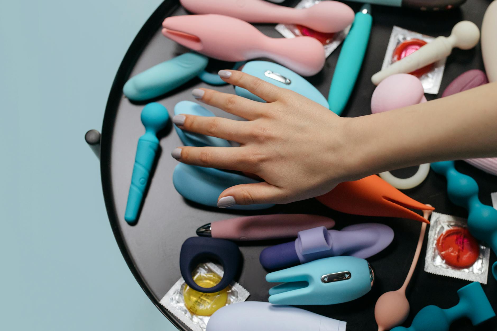 A hand reaching over a variety of colorful lemon sexual toys arranged on a table.