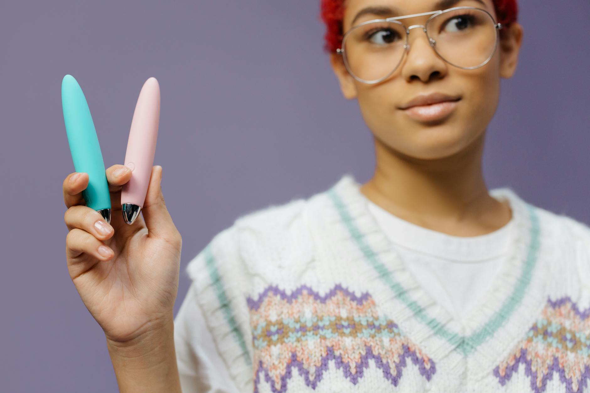 A woman holding two colorful vibrators against a purple background, symbolizing reclaiming pleasure