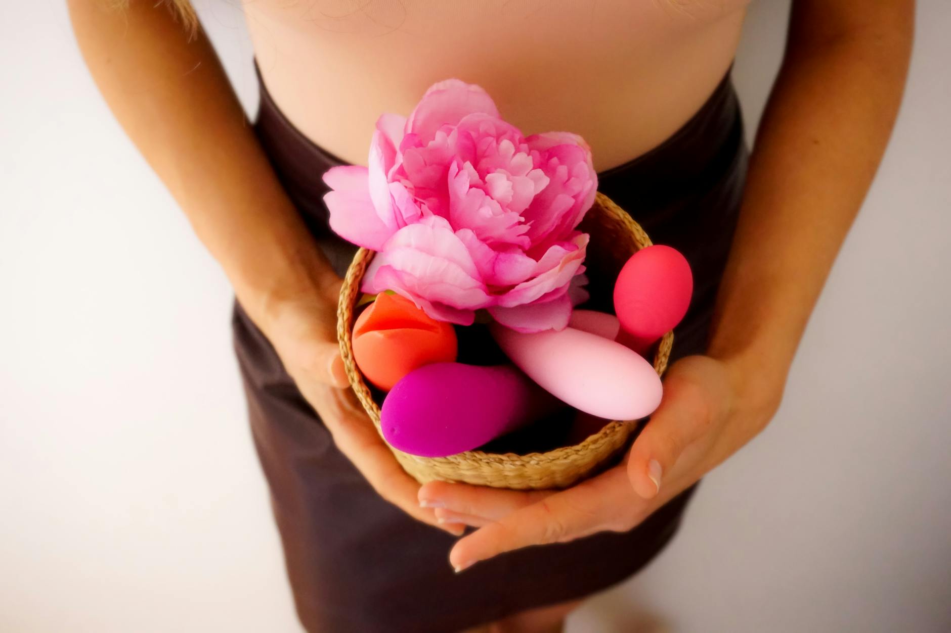 Colorful vibrators in a basket with fresh flowers, representing pleasure and wellness tools
